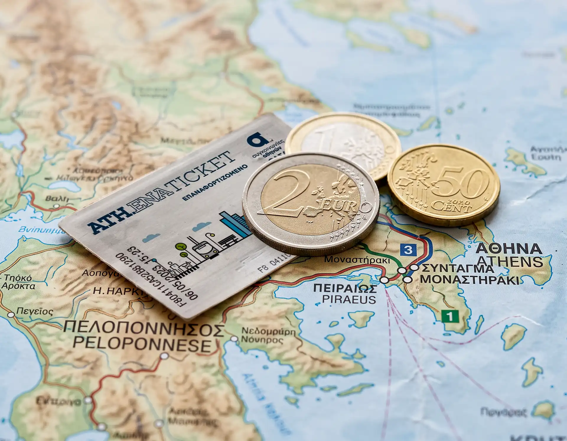Monedas de euro y billete de metro de Atenas sobre un mapa de Grecia